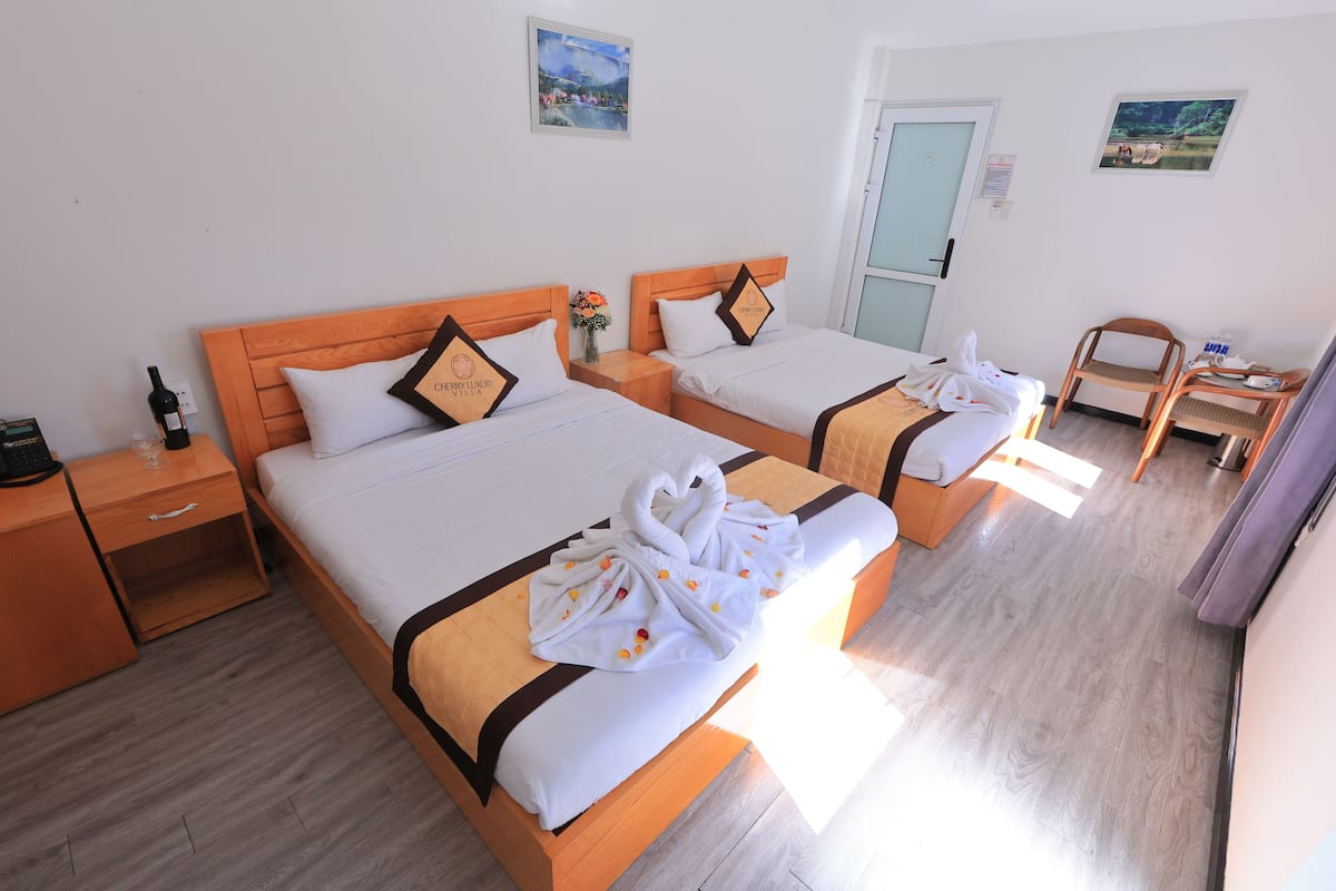 A hotel room with two beds, wooden headboards, white bedding, and a wooden floor.