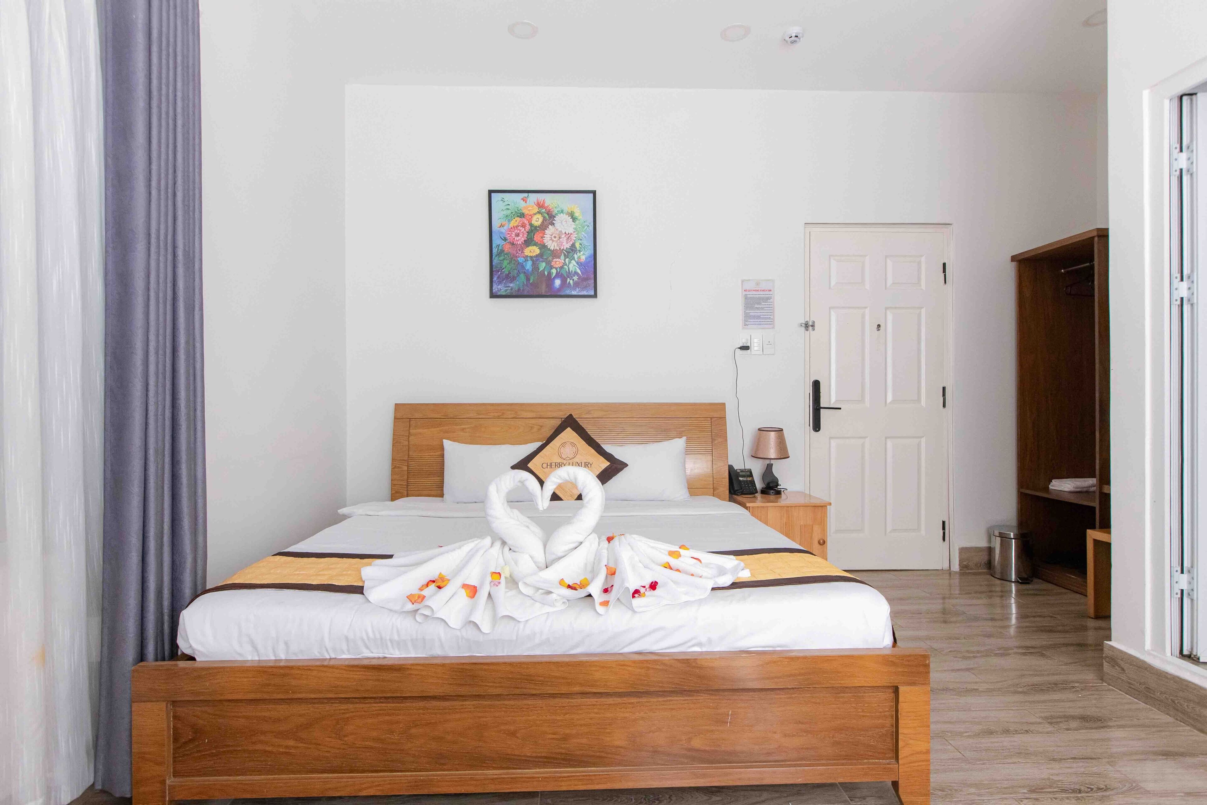A hotel room with a wooden bed, a painting on the wall, a door, and a wardrobe.