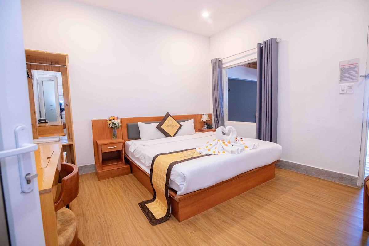 A hotel room with a wooden bed, a nightstand, a desk, and a chair.