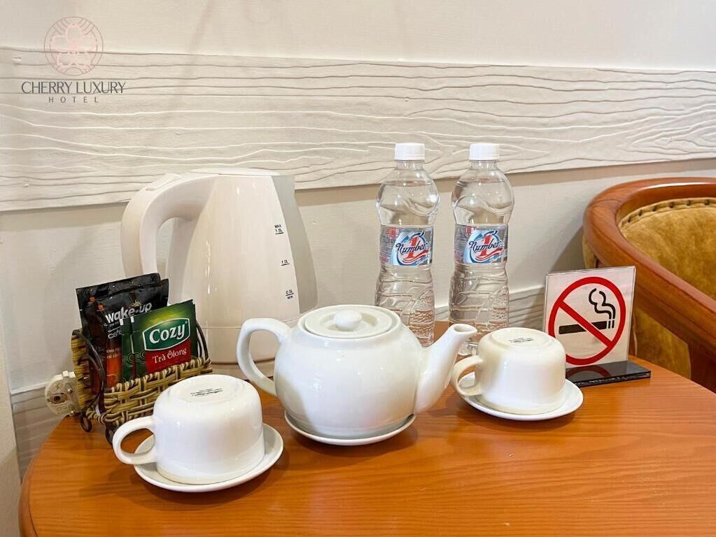 Habitación de hotel con una mesa de madera dispuesta con tetera, tazas y agua embotellada. También hay cápsulas de café y un cartel de prohibido fumar en la pared.