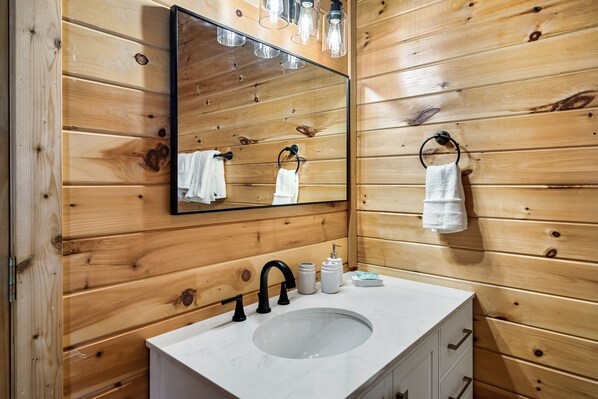 Un baño con paneles de madera, un lavabo blanco y un grifo negro, con un espejo encima.