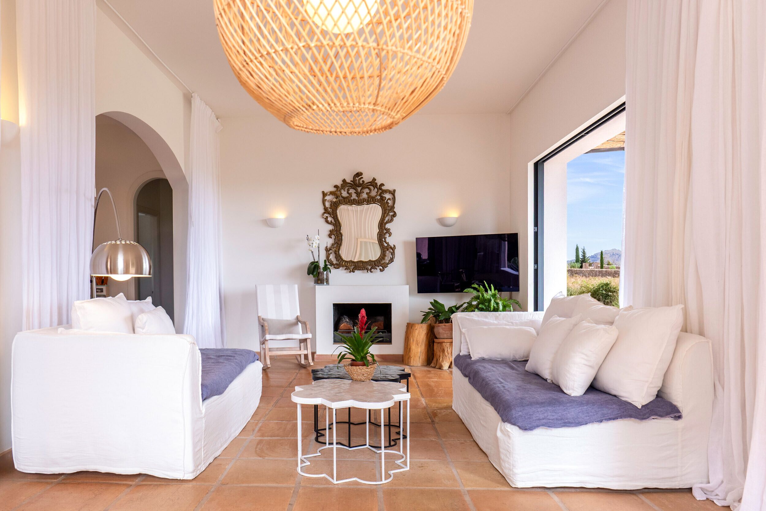 Ein modernes Wohnzimmer mit weißen Sofas, einem weißen Couchtisch und einer großen, gewebten Pendelleuchte.