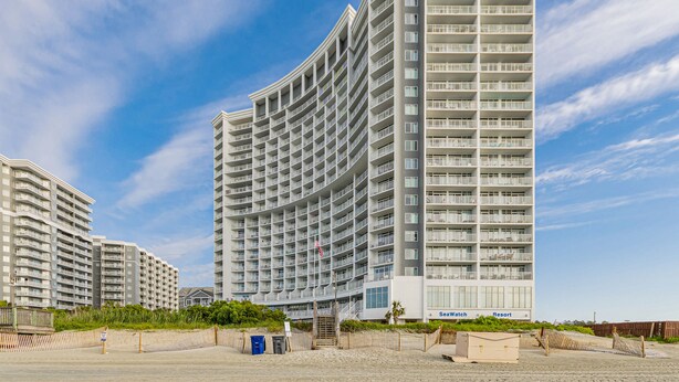 A multi-story hotel with a curved facade, balconies, and a beach view.