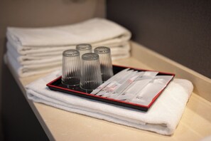 A stack of white towels and a tray with four glass bottles and a red tray on a beige surface. - Rich & Free Hotel Kaifeng (Taipei)