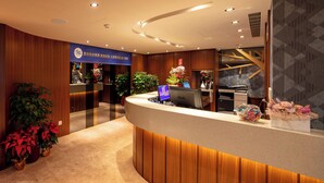 A modern reception area with a curved reception desk, wooden paneling, and potted plants. - Rich & Free Hotel Kaifeng (Taipei)