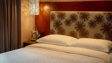 A hotel room with a bed, a nightstand, a lamp, and a wall with a floral pattern.