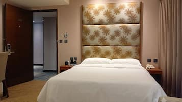 A hotel room with a large bed, a headboard with a floral pattern, bedside tables with lamps, and a door with a number.