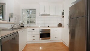 A modern kitchen with white cabinets, stainless steel appliances, and a wooden floor. - Unit 4 'Marcoola Sands' on Petrie Avenue (Marcoola)