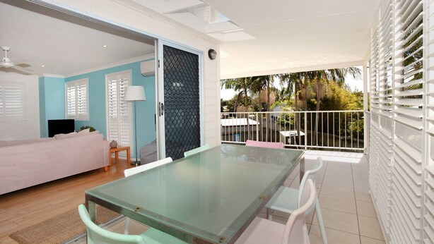 A modern living room with a glass table and chairs, a sofa, and a sliding glass door leading to a balcony with a view of palm trees. - Unit 4 'Marcoola Sands' on Petrie Avenue (Marcoola)