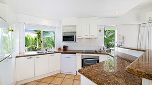 A modern kitchen with white cabinets, a granite countertop, a built-in microwave, and a dishwasher. - Unit 8.12 Perry Street (Coolum Beach)