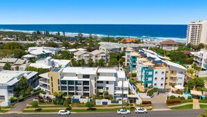 A coastal residential area with modern apartment buildings, a clear view of the ocean, and a well-maintained green space in the foreground. - Unit 8.12 Perry Street (Coolum Beach)