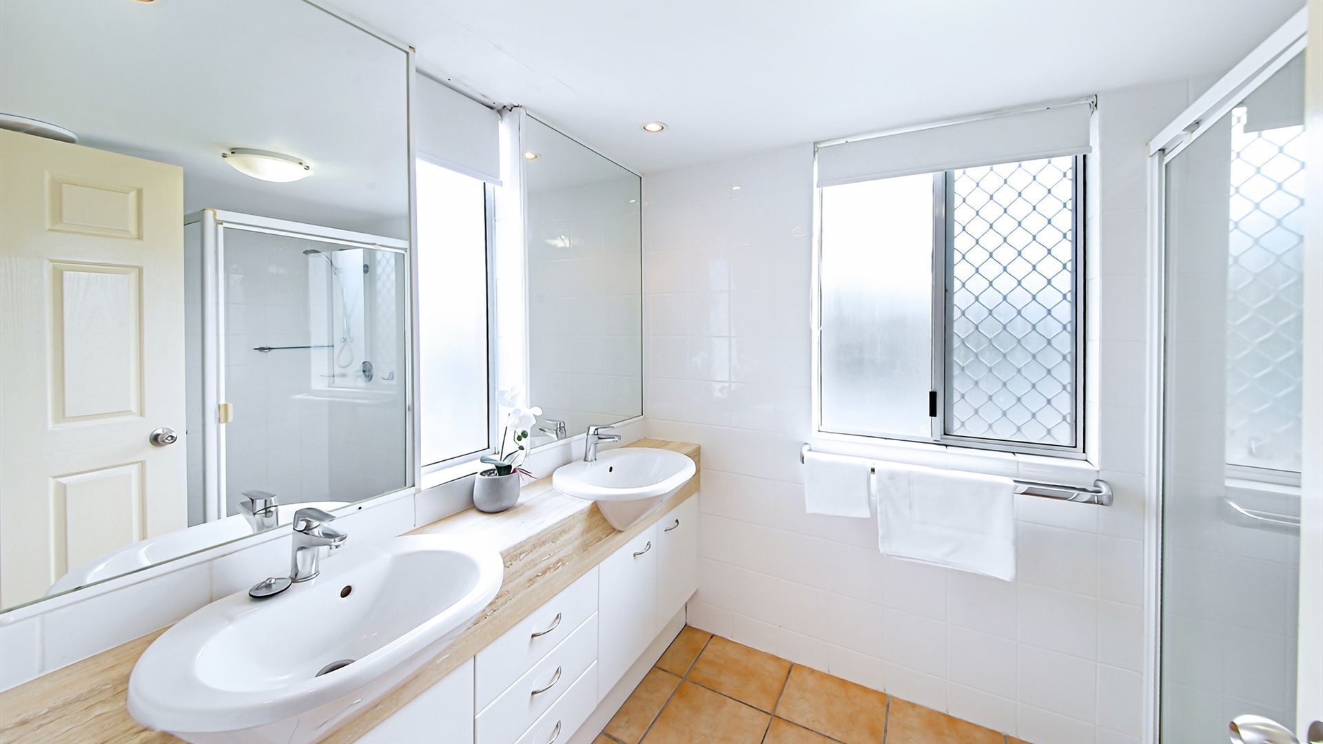 A modern bathroom with two sinks, a large mirror, and a window with a diamond-patterned blind.