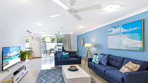 A modern living room with a large TV, a sofa, a coffee table, and a painting of a beach scene.