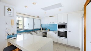 A modern kitchen with white cabinets, a large island, a microwave, and an oven. - Central Coolum Penthouse with Rooftop Terrace (Coolum Beach)