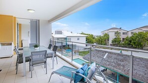 A balcony with a glass railing, a dining table with chairs, a small pool, and a view of neighboring houses. - Central Coolum Penthouse with Rooftop Terrace (Coolum Beach)