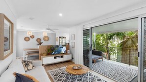 A modern living room with a large TV, wooden furniture, and a balcony with a view of greenery. - Unit 2 'Marcoola Sands' (Marcoola)