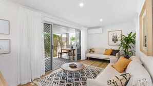 A modern living room with a sofa, coffee table, and a dining area with a table and chairs. - Unit 2 'Marcoola Sands' (Marcoola)
