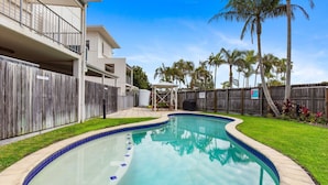 A swimming pool with a wooden deck, surrounded by a wooden fence and palm trees. - Unit 2 'Marcoola Sands' (Marcoola)