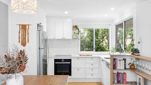 A modern kitchen with white cabinetry, a Bosch oven, and a large window offering a view of greenery. - Unit 2 'Marcoola Sands' (Marcoola)