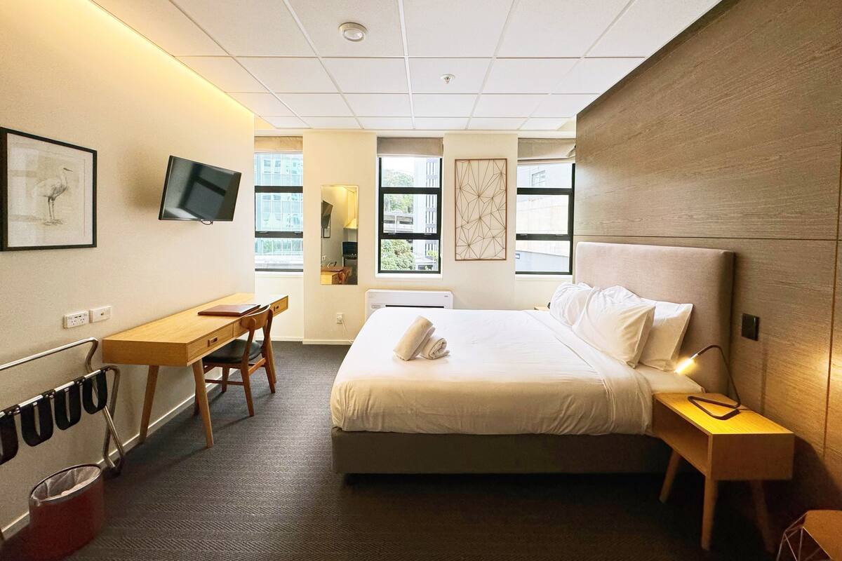 Una habitación de hotel con cama, escritorio, silla, televisor y ventana.