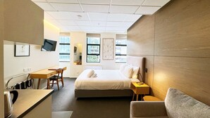 A hotel room with a bed, a desk, a chair, a sofa, and a TV mounted on the wall.