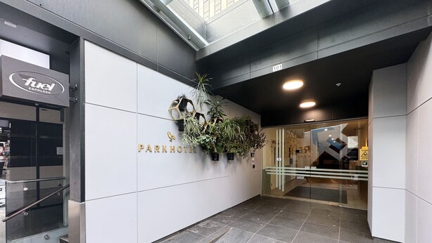 A modern hotel entrance with a clean, white facade, a sign for 'Park Hotel', and a 'Fuel Espresso' shop to the left.