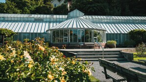 A greenhouse with a glass dome structure, surrounded by a garden with various plants and flowers.