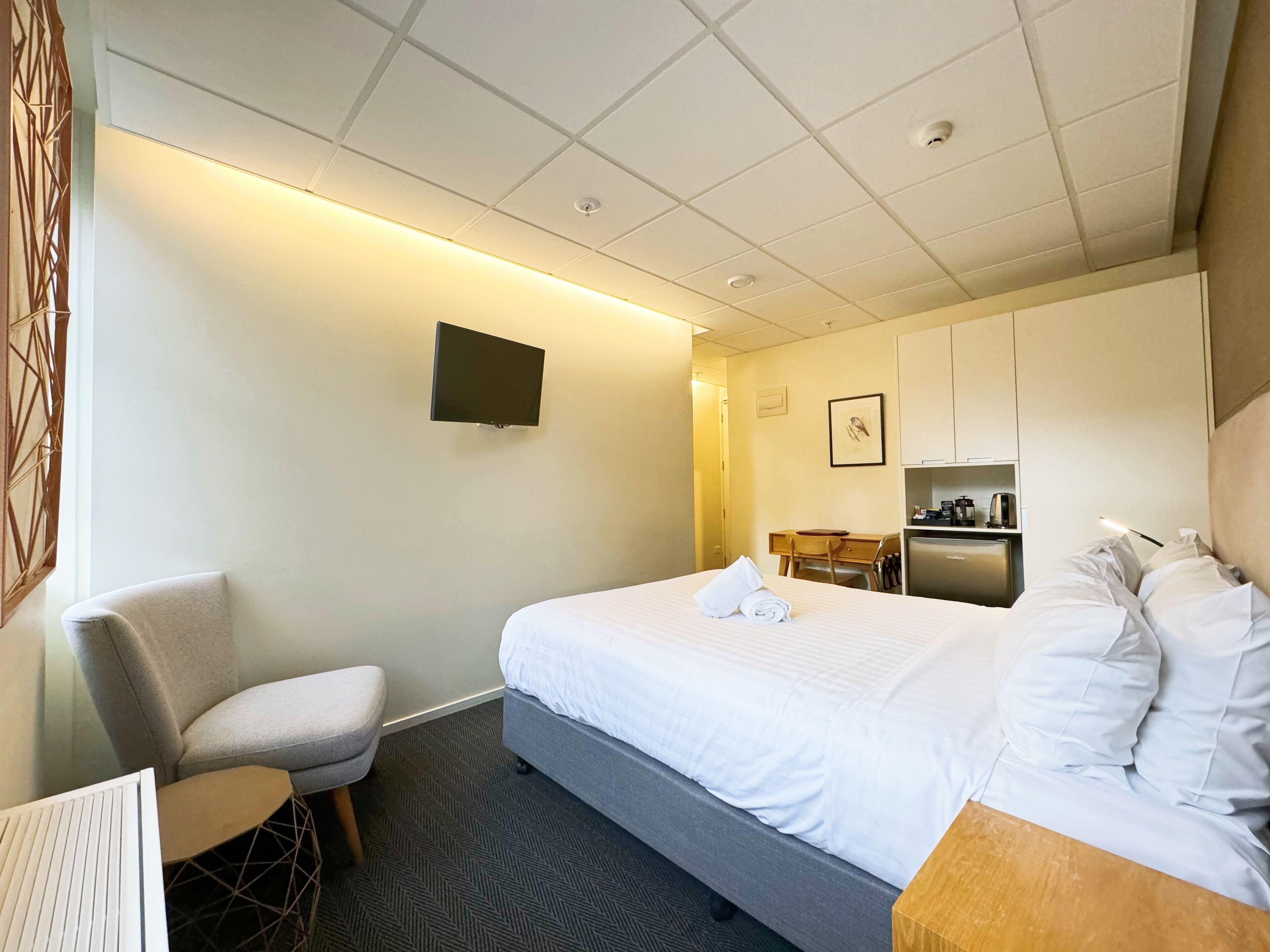 Ein Hotelzimmer mit Bett, Schreibtisch, Stuhl, Fernseher und einer Küchenzeile.