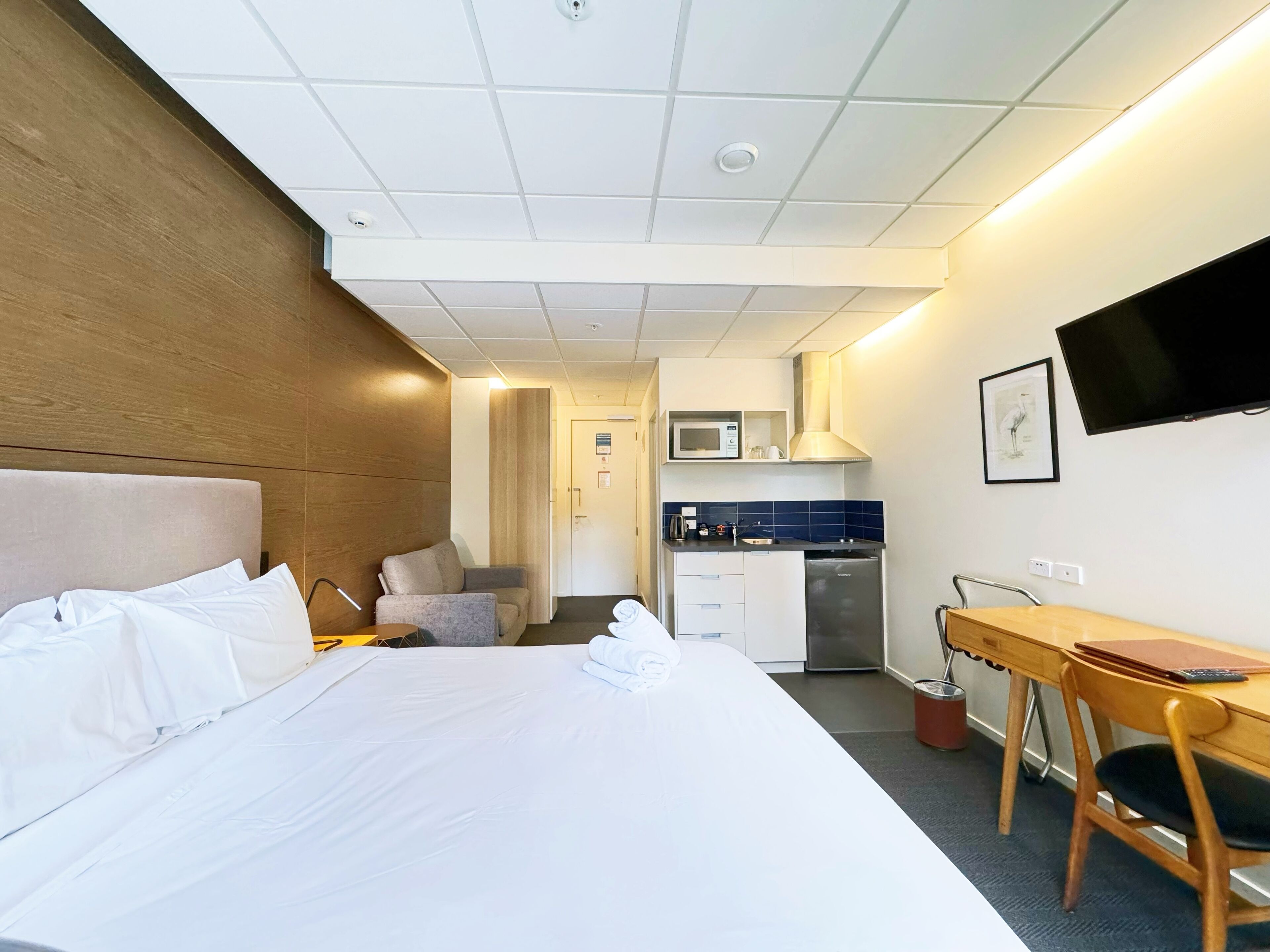 Ein Hotelzimmer mit Bett, Schreibtisch, Stuhl, Küchenzeile und Fernseher.
