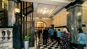 A lobby with a checkered floor, marble columns, and a staircase with a metal railing.
