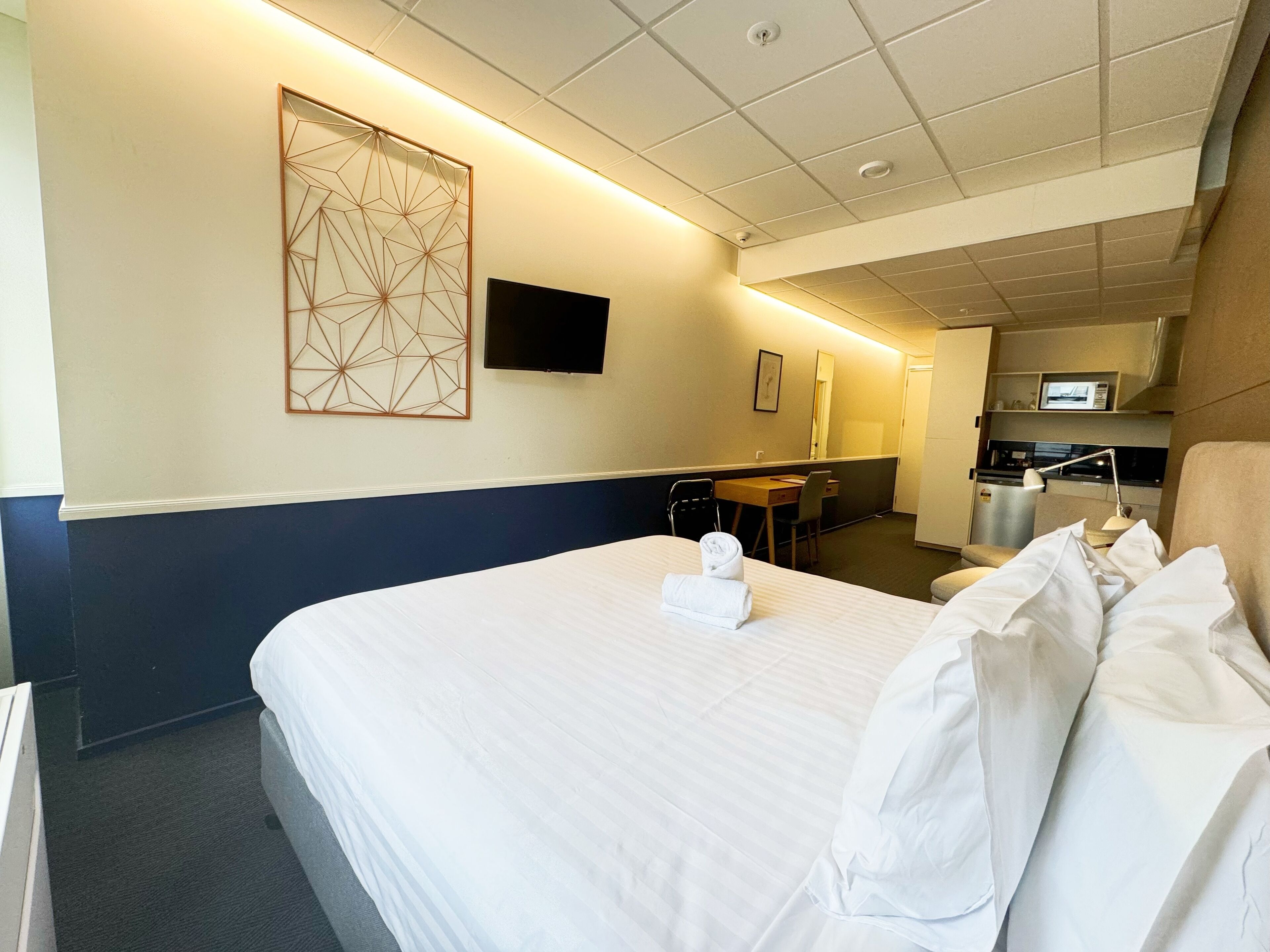Une chambre d’hôtel avec un grand lit, un bureau, une chaise, une télévision et une kitchenette.