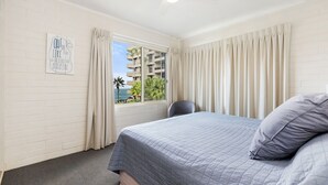 A hotel room with a bed, a chair, a window with curtains, and a sign on the wall.