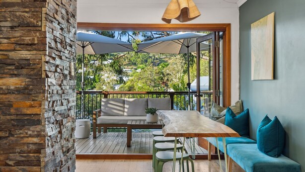 A balcony with a wooden table, a sofa, and a potted plant. - Cottage on Lorien Avenue (Coolum Beach)
