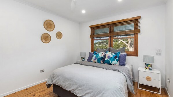 Un dormitorio con cama, mesita de noche, ventana con persianas y tres placas decorativas en la pared.