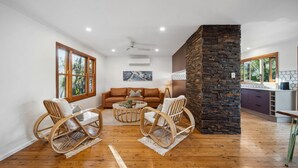 A spacious living area with a brown leather sofa, wicker chairs, a coffee table, and a stone accent wall. - Cottage on Lorien Avenue (Coolum Beach)