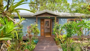 A house with a wooden front door, a number 21 sign above it, and a wooden pathway leading to the entrance. - Cottage on Lorien Avenue (Coolum Beach)