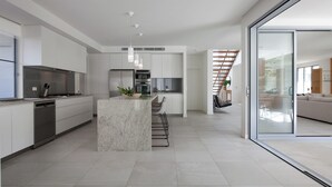 Una cuina moderna amb una illa central, electrodomèstics integrats i una porta de vidre que dona a una zona d'estar.