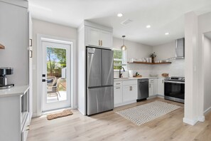 Une cuisine moderne avec des meubles blancs, des appareils en acier inoxydable et une vue sur l’extérieur.