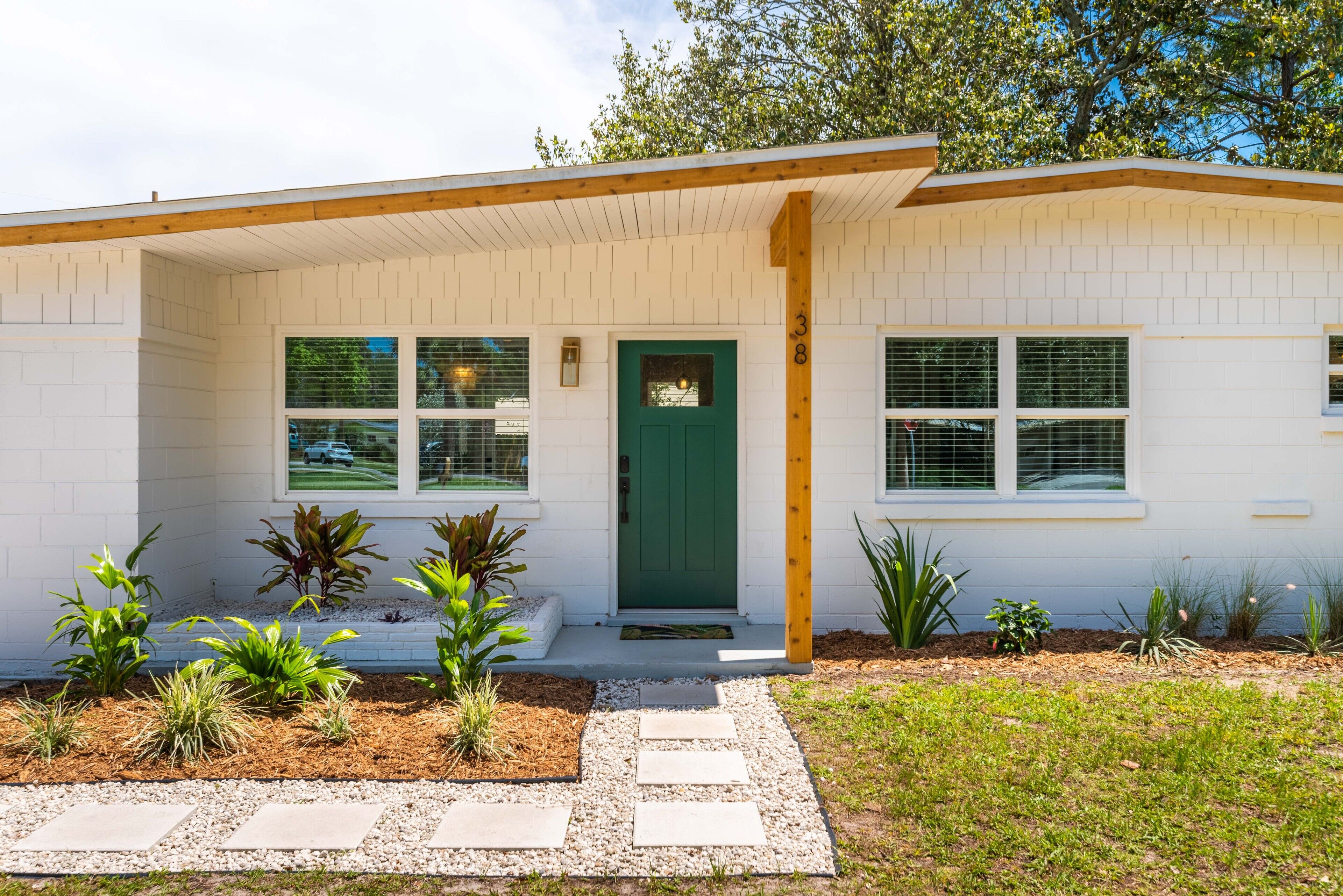 A modern single-story house with a green door, white exterior walls, and a small front porch.