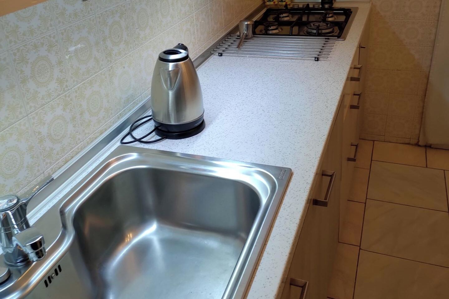 Een keuken met een RVS spoelbak, een waterkoker en een gasfornuis.