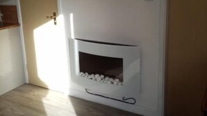 A room with a flat-screen TV mounted on the wall, a fireplace with a stone surround, and wooden flooring. - Chalet Retreat in Mablethorpe (Mablethorpe)