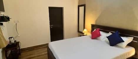 Un dormitorio con cama, ventilador de techo, unidad de aire acondicionado, puerta y mesita de noche con lámpara.
