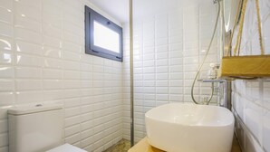 A bathroom with white tiled walls, a white toilet, a wooden vanity with a white sink, and a shower area. - Mediterranean House in Badalona (Badalona)