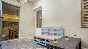 A small outdoor seating area with a wooden bench and a wicker table, a potted plant, and a view into a kitchen area. - Mediterranean House in Badalona (Badalona)