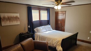 Une chambre à coucher comprenant un lit, une table de chevet, un bureau, une chaise, un ventilateur de plafond et une porte.