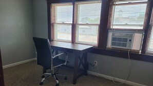 Une pièce avec un bureau en bois, un fauteuil de bureau noir et une fenêtre avec des stores.