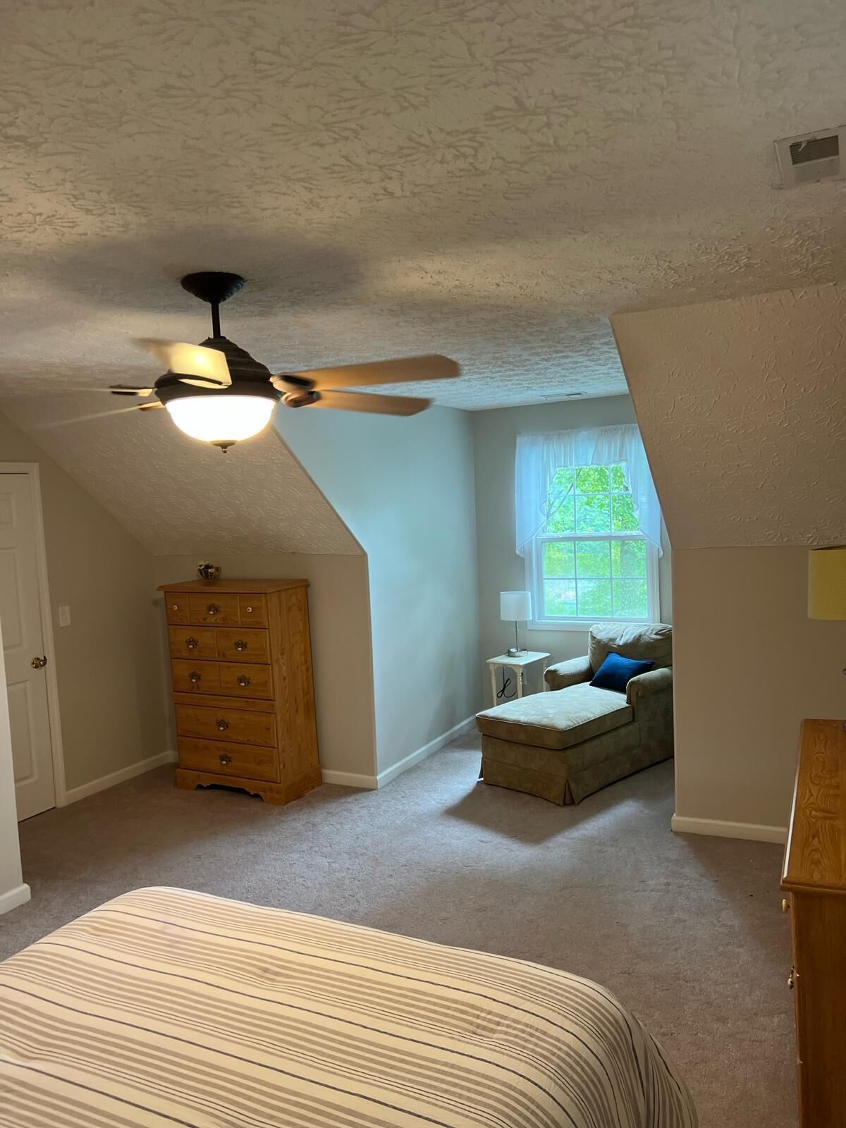 A bedroom with a ceiling fan, a dresser, a window with a view, and a couch.