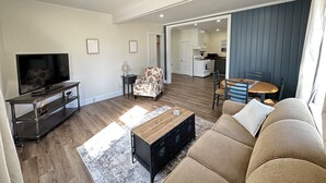 Una sala de estar moderna con televisor de pantalla plana, sofá, mesa de centro y comedor con mesa y sillas de madera.