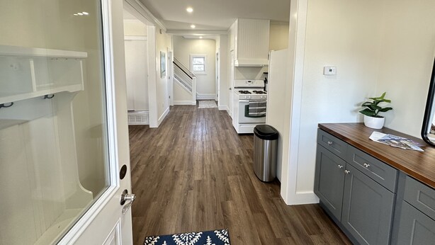 Un pasillo que conduce a una cocina con piso de madera, armarios blancos y un cubo de basura de acero inoxidable.
