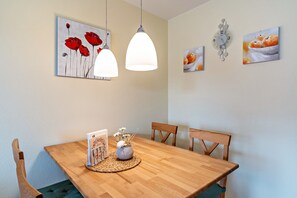 Un coin repas avec une table en bois, deux lampes suspendues, un vase de fleurs et des œuvres d’art murales.